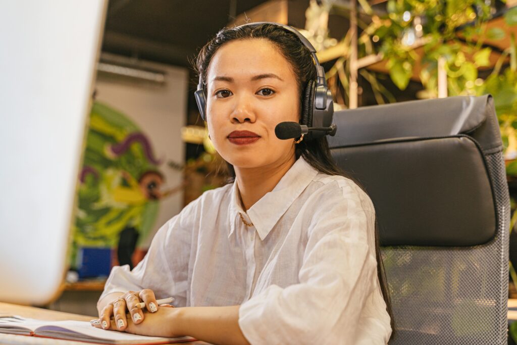 Asian woman in office wearing headset, working in a modern call center environment.